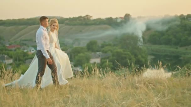 La pareja de boda se comunica en el fondo del cielo, la novia con un ramo de flores. de pie sobre una roca. — Vídeos de Stock