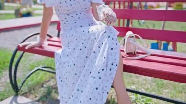 Mutlu genç bir kadın parkta arka planda kırmızı bir telefon kulübesinde oturuyor ve gözlüklerini düzeltiyor. Etrafa bakıyorum. pinup.