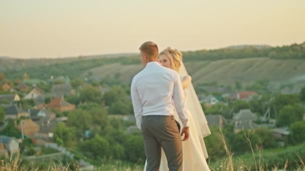 Het bruidspaar communiceert op de achtergrond van de hemel, de bruid met een boeket bloemen. staand op een rots. — Stockvideo