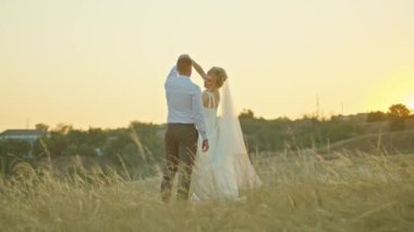 Düğün çifti gökyüzünün arka planında iletişim kuruyor, gelin elinde bir buket çiçekle. Bir kayanın üzerinde duruyor.