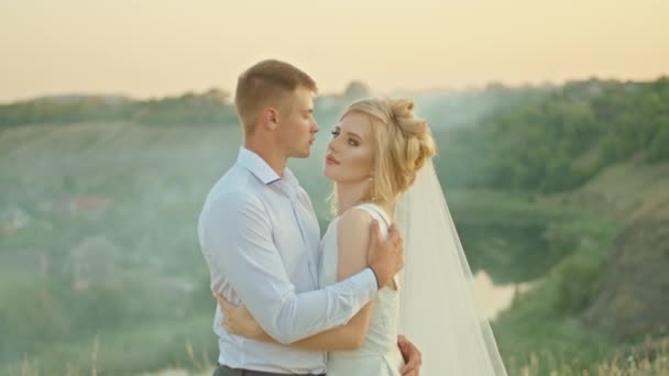 Das Hochzeitspaar kommuniziert auf dem Hintergrund des Himmels, die Braut mit einem Blumenstrauß. auf einem Felsen stehend. — Stockvideo
