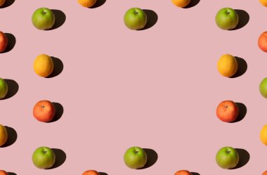 Renkli yaz meyveleri taze organik yeşil elmalar, limonlar ve pembe pastel arka planda mandalinalı portakallar. Karşıt asgari geometrik konsept.