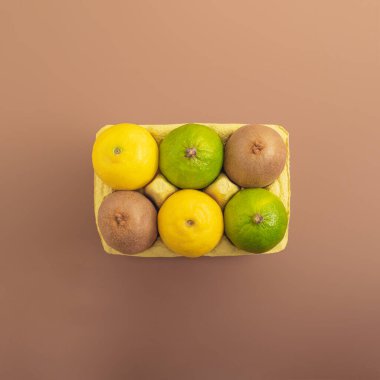 Minimalist vegan gıda fikri, basit kahverengi arka plan. Yumurta paketinde taze organik limon, limon ve kivi. Yaratıcı meyve yaz konsepti, düzleştirme.