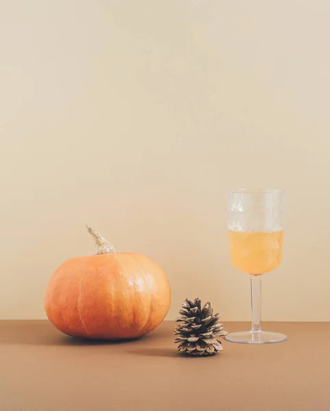 Retro style aesthetic concept with a pumpkin, pine and drinking glass on pastel brown background. Creative 2021 Halloween and autumn idea, minimalistic vertical arrangement.