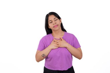 Latin Latin kadın, rahat ve sakin, mor bir tişört giyiyor, beyaz arka planda izole edilmiş, ellerini göğsüne koyuyor, sakin bir ifadeyle..