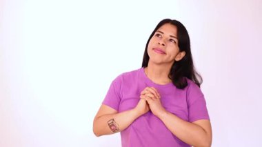 Latin Latin bir kadın, rahat ve sakin, mor bir tişört giyiyor, beyaz arka planda izole edilmiş, sakin bir ifadeyle ellerini göğsüne yakın tutuyor..