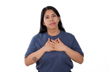 Latin Latin bir kadın, rahat ve sakin, beyaz arka planda izole edilmiş mavi bir tişört giyiyor, sakin bir ifadeyle ellerini göğsüne koyuyor..