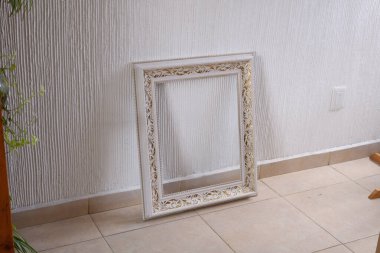 Kaliteli kare çerçeve, beyaza boyanmış altın yapraklı detaylar, desenli beyaz bir duvara yaslanmış ve döşenmiş. Kopya, tasarım ve iç dekorasyon için boş boşluk.