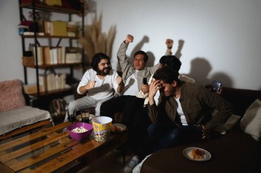 Kanepedeki dört genç adam ekrana aşırı tepki veriyor. İki sevinçle, biri kutlar, diğeri yüzünü saklar. Eğlence sırasında karşıt duygusal tepkileri yakalar