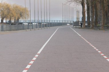 Ağaçlarla çevrili göl kenarındaki şehir seti boyunca beyaz çizgileri olan boş asfalt kaldırım. Seyahat, tasarım ve mimari kavramlar için şehir manzarası arka planı.