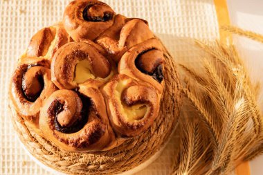 Kremalı çörek ve saman standında buğday kulaklı kuru üzüm. Sıcak tatlı pasta konforu, tazeliği ve geleneksel ev pişirmesini simgeler..