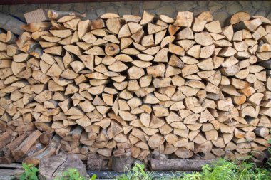 Stack of chopped firewood logs neatly arranged outdoors against stone wall. Concept of renewable energy, rural life, and natural resources.