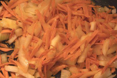 Sliced carrots and onions fried in a pan. Cooking vegetables for homemade food, soup, or stew. Natural warm light and healthy meal preparation.