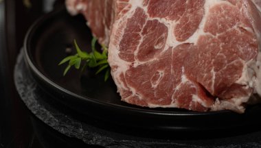 Yeşil otlu siyah tabakta taze çiğ domuz eti dilimi. Yemek pişirme, protein besin ve mutfak hazırlığı kavramı.