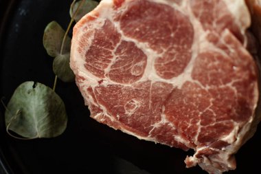 Yeşil otlu siyah tabakta taze çiğ domuz eti dilimi. Yemek pişirme, protein besin ve mutfak hazırlığı kavramı.