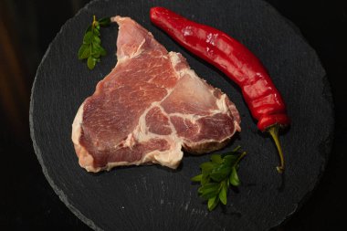 Kırmızı biberli taze çiğ domuz dilimi ve siyah tahtada yeşil otlar. Yemek pişirme, malzemeler ve sağlıklı protein yiyeceği kavramı.