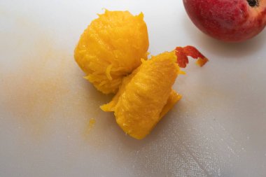 Meyvenin yanına beyaz bir kesme tahtasına yerleştirilmiş parlak sarı renkli sulu şeftali posası..