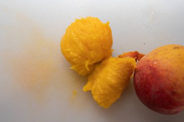 Meyvenin yanına beyaz bir kesme tahtasına yerleştirilmiş parlak sarı renkli sulu şeftali posası..