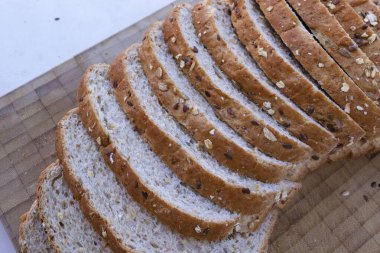 Tahta kesme tahtasının üzerinde yulaf ve tohumla dilimlenmiş taze tahıl ekmeği, sağlıklı fırın ürünü..