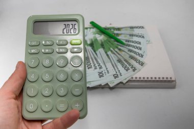 2026 yılını gösteren hesap makinesi. Avro banknotları ve beyaz arka planda yeşil kalemle. Yeni yıl için mali planlama, iş hedefleri ve bütçe kavramı.