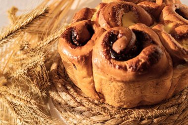 Sıcak gün ışığında altın buğday kulaklarının yanında hasırın üzerine konmuş reçelli ve kremalı taze ev yapımı tatlı çörekler.