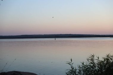 Sakin nehrin üzerinde parlak turuncu yansımalarla huzurlu bir gün batımı..