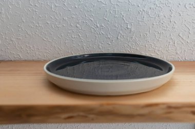 Ahşap rafta dokulu duvara karşı boş siyah beyaz seramik tabak.