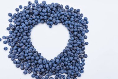 Temiz beyaz arka planda kalp şeklinde dizilmiş taze yaban mersini.