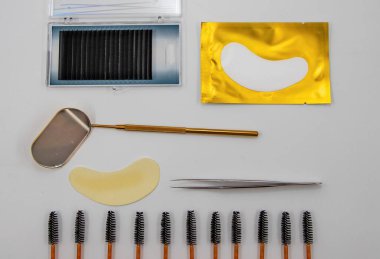 Profesyonel kirpik uzatma araçları beyaz arkaplanda düzgünce düzenlenmiş fırçalar, yamalar cımbızlar ve palet