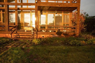 Günbatımının ılık ışığıyla aydınlatılmış geniş pencereli modern ahşap iki katlı bir ev.