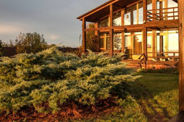 Günbatımının ılık ışığıyla aydınlatılmış geniş pencereli modern ahşap iki katlı bir ev.