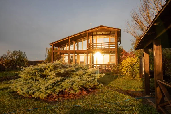 Günbatımının ılık ışığıyla aydınlatılmış geniş pencereli modern ahşap iki katlı bir ev.
