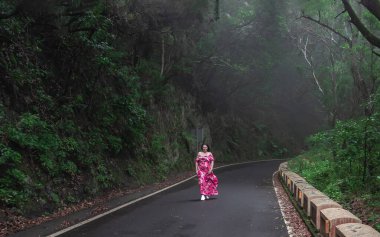 Sisli Tenerife Ormanı yolunda tek başına yürüyen bir kadın yemyeşil doğa ile çevrili.