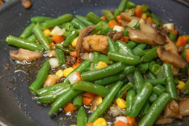 Yeşil fasulyeli sebze, tavada pişmiş mısır havucu ve mantar karışımı.