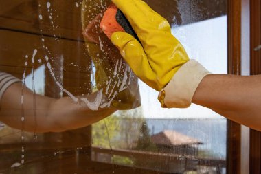 Ev temizliği sırasında sarı eldivenli ve süngerli el temizleme camı.