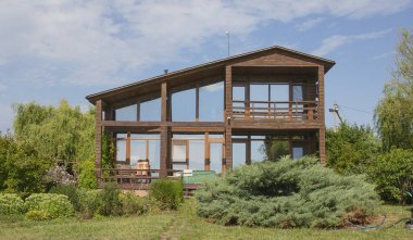 Yeşil yaz bahçesiyle çevrili büyük cam pencereli modern ahşap kır evi.