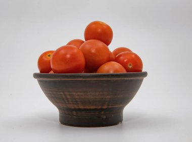 Kırsal seramik kasede taze olgun domatesler temiz beyaz stüdyo arka planına yerleştirilmiş.