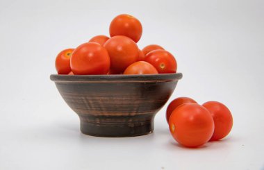 Kırsal seramik kasede taze kırmızı domatesler ve temiz arka planda gevşek meyveler.