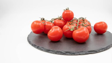 Koyu tabakta taze vişneli domatesler. Yemek pişirmek için beyaz arka plana yerleştirilmiş.