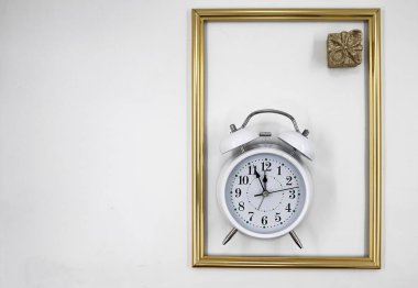 Altın çerçevenin içinde küçük bayram hediyeli beyaz klasik çalar saat bayram konsepti yaratıyor.