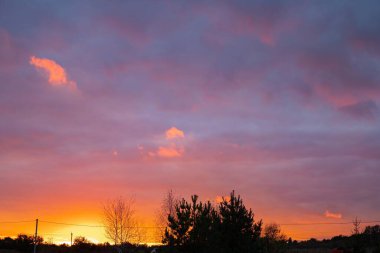 Parlayan turuncu ufuk ve manzaranın üzerinde yumuşak mor bulutlar ile canlı günbatımı gökyüzü