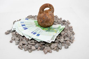 Gri çakıl taşı üzerindeki avro banknotlarına baskı yapan paslı metal ağırlığı sembolik mali konsept oluşturuyor