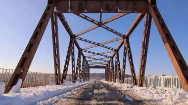 Kar, kış manzaralı metal köprü yapısını ve açık mavi gökyüzünü kapladı.