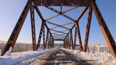 Kar, kış manzaralı metal köprü yapısını ve açık mavi gökyüzünü kapladı.