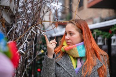 Soğuk festival sezonunda kış ağacı dallarını renkli eşarplarla inceleyen genç bir kadın.