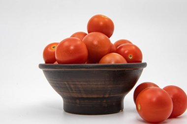 Taze kırmızı domatesler, temiz beyaz stüdyo arka planında sade ahşap kasede dizilmiş.