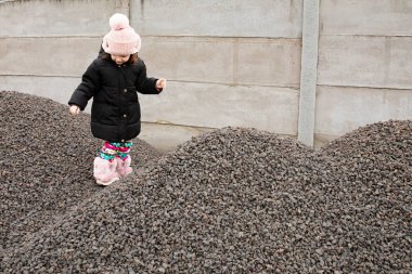 Soğuk kış gününde beton duvarın yanında çakıl tepesinde yürüyen küçük bir kız.