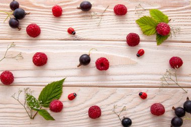 Taze ahududu ve yeşil yapraklar, açık ahşap zemin üzerine saçılmış.