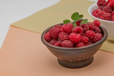 Pastel arka planda seramik kaselerde taze ahududu ve fotokopi alanı.