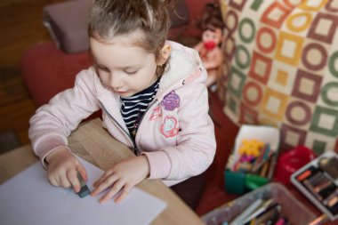 Sessiz yaratıcı ev aktivitesi sırasında masada kalemle çizim yapan küçük bir kız.